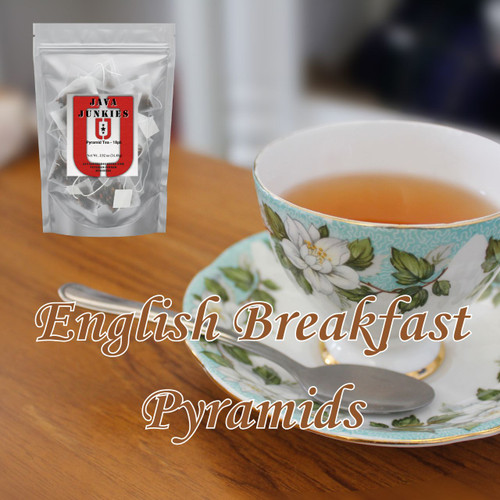 An ornate white floral teacup filled with amber English Breakfast tea beside a silver spoon resting on a polished wooden tabletop.