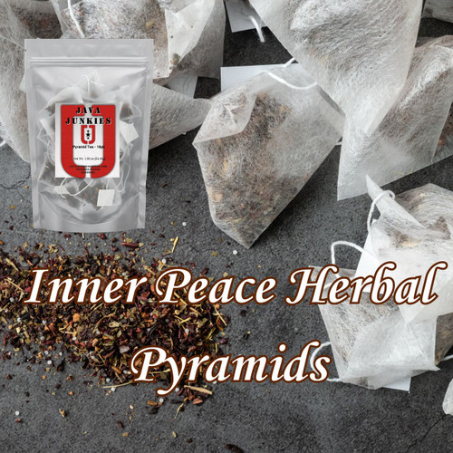 Several white pyramid tea bags alongside loose dried herbal leaves and floral pieces scattered across a dark textured surface.
