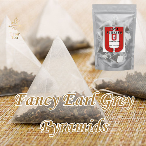 A prominent mesh pyramid tea bag filled with dark tea leaves resting on a woven mat, accompanied by a retail packaging pouch.