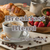 Java Junkies Breakfast Blend Coffee. Coffee cup full of coffee on a saucer next to some fresh strawberries and pastries sitting on a table with cream.
