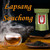 A double-walled glass cup filled with amber tea surrounded by rising smoke, a dark teapot, and a small dish of loose black tea leaves on a wooden table.