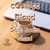 Java Junkies eCoffee Blend Coffee. White modern coffee mug filled with creamy coffee on a wood coaster next to a laptop.