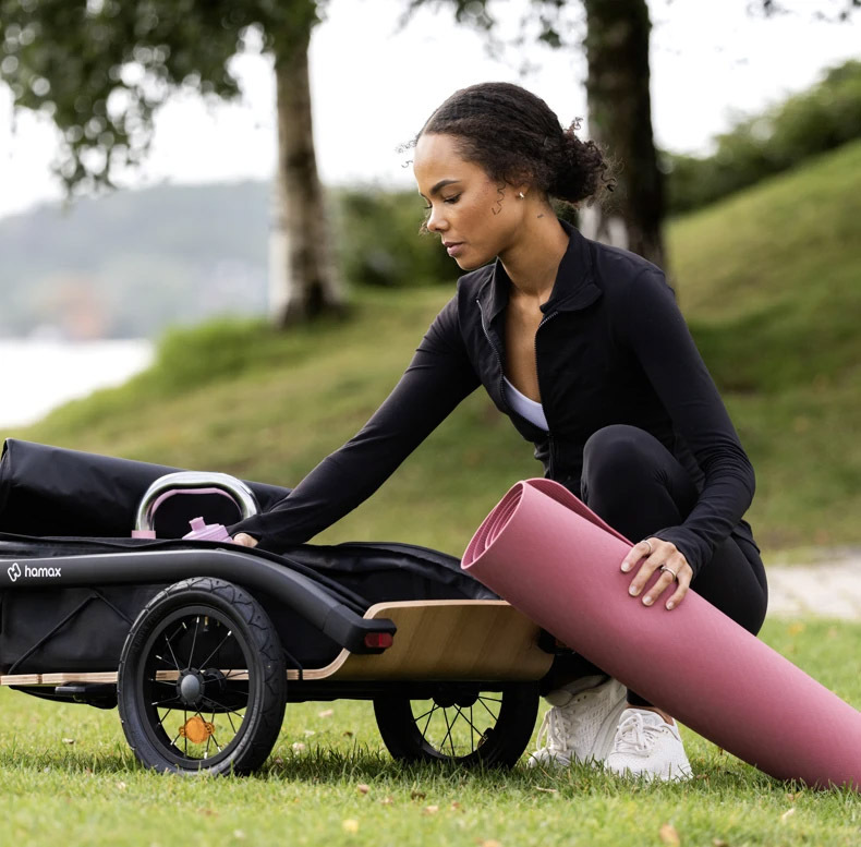 Person loading a rolled yoga mat into a Hamax Venture trailer on grass