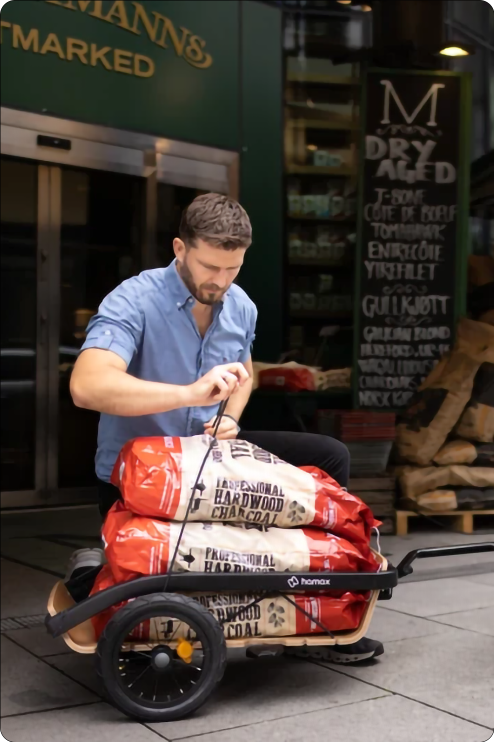 Person securing bags of charcoal in a Hamax Venture trailer outside a shop