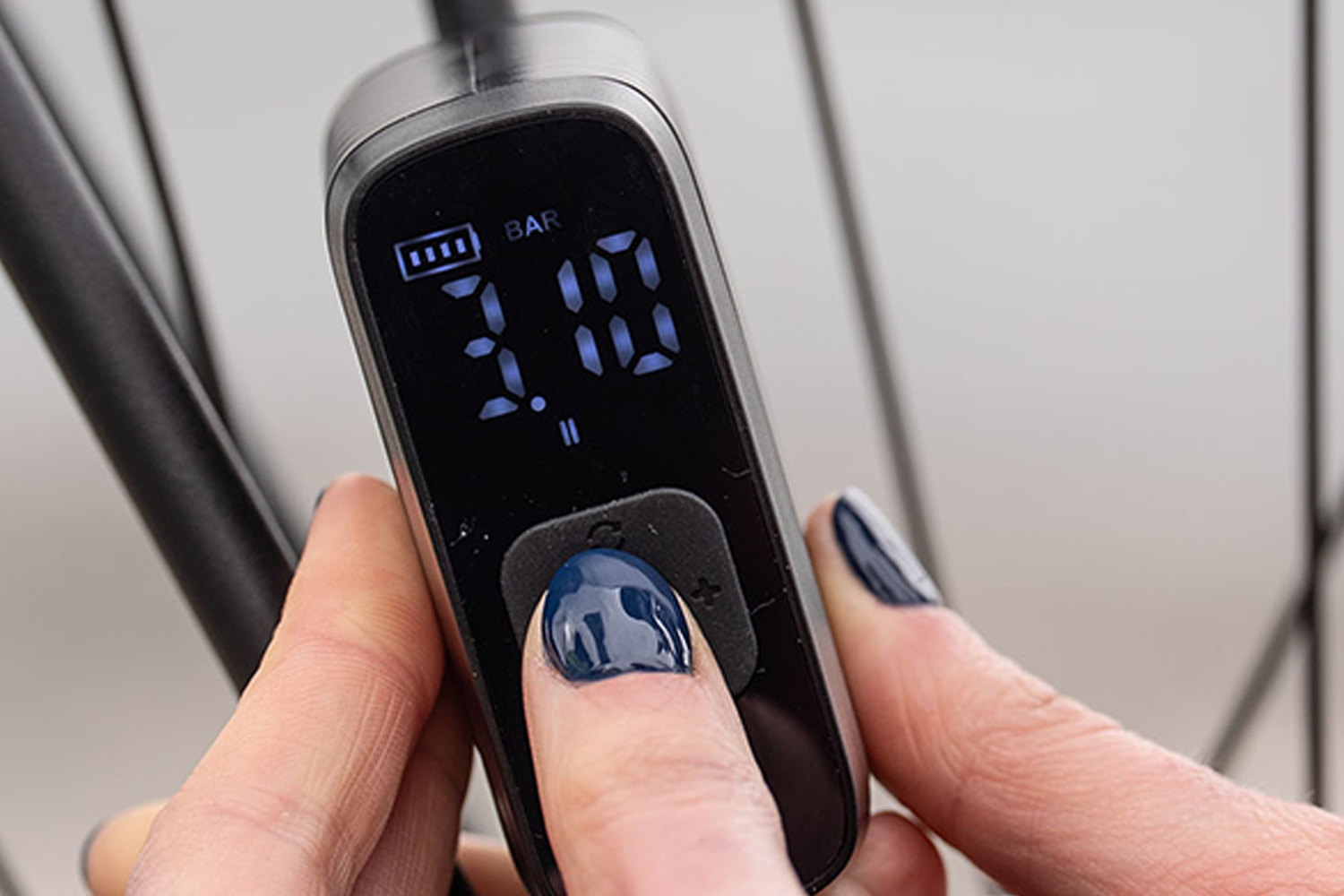 Close-up of the BBB Cycling BarBank digital display showing tyre pressure settings while being adjusted beside a bicycle wheel. 