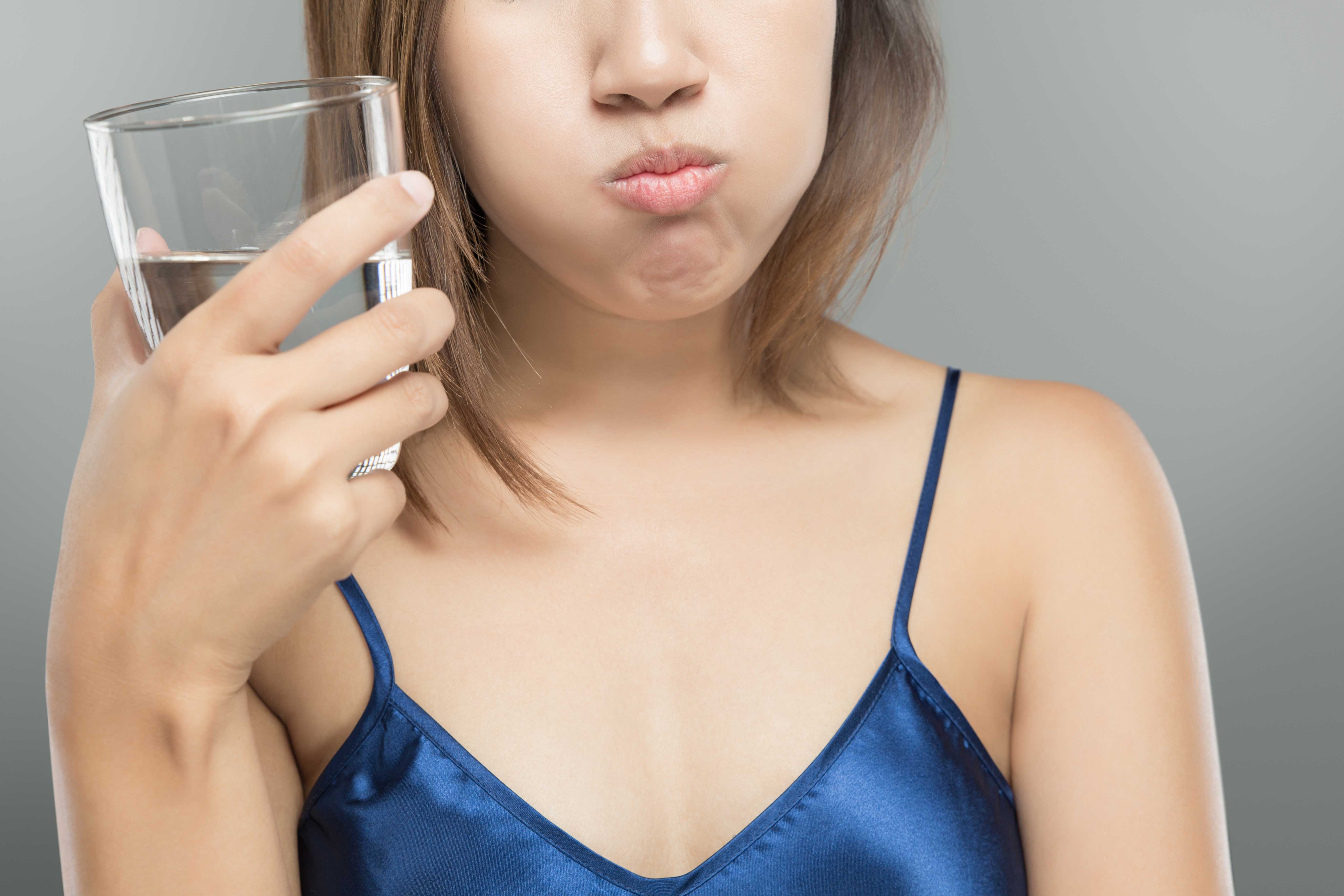 Woman rinsing with mouthwash and holding glass of water