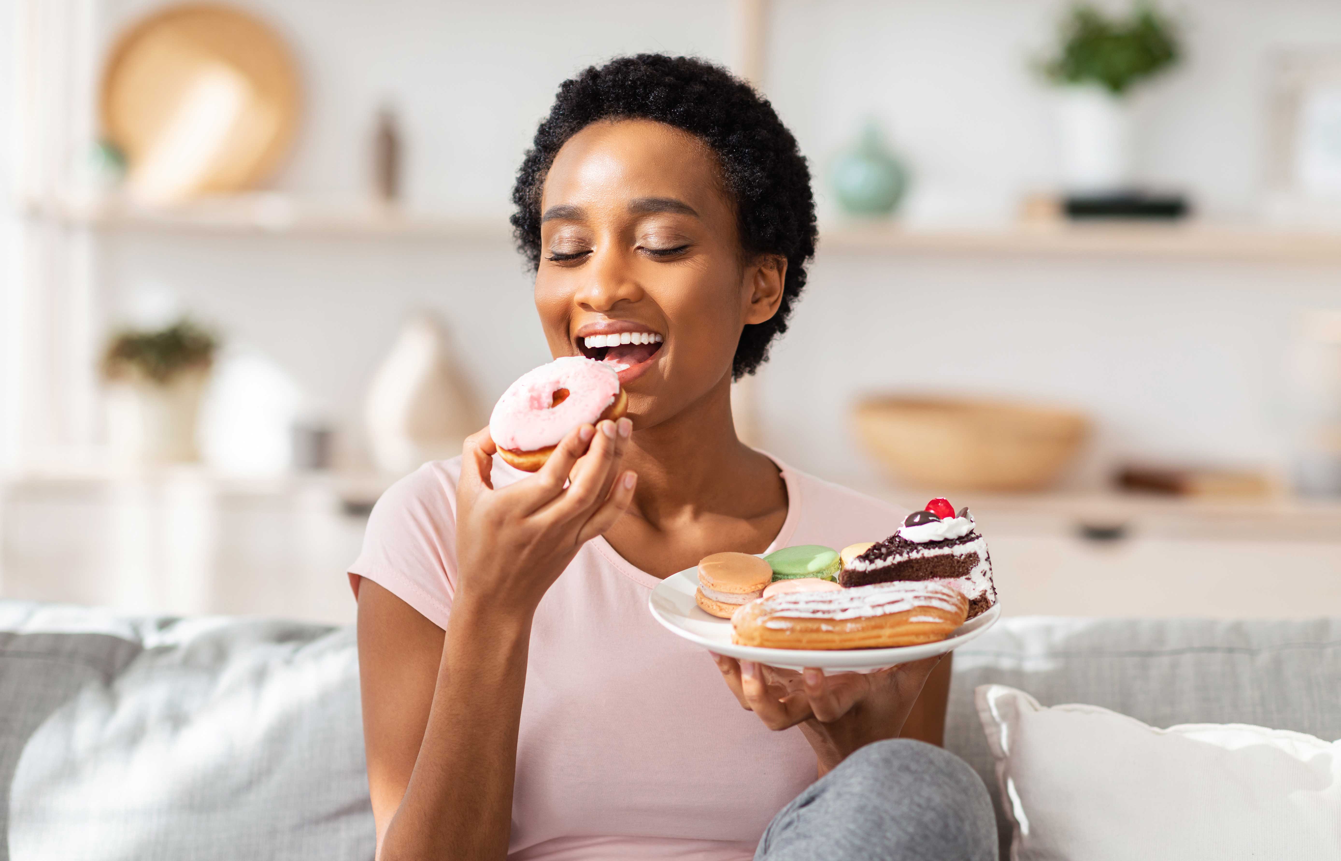 Woman eating a donut and holding a plate of desserts