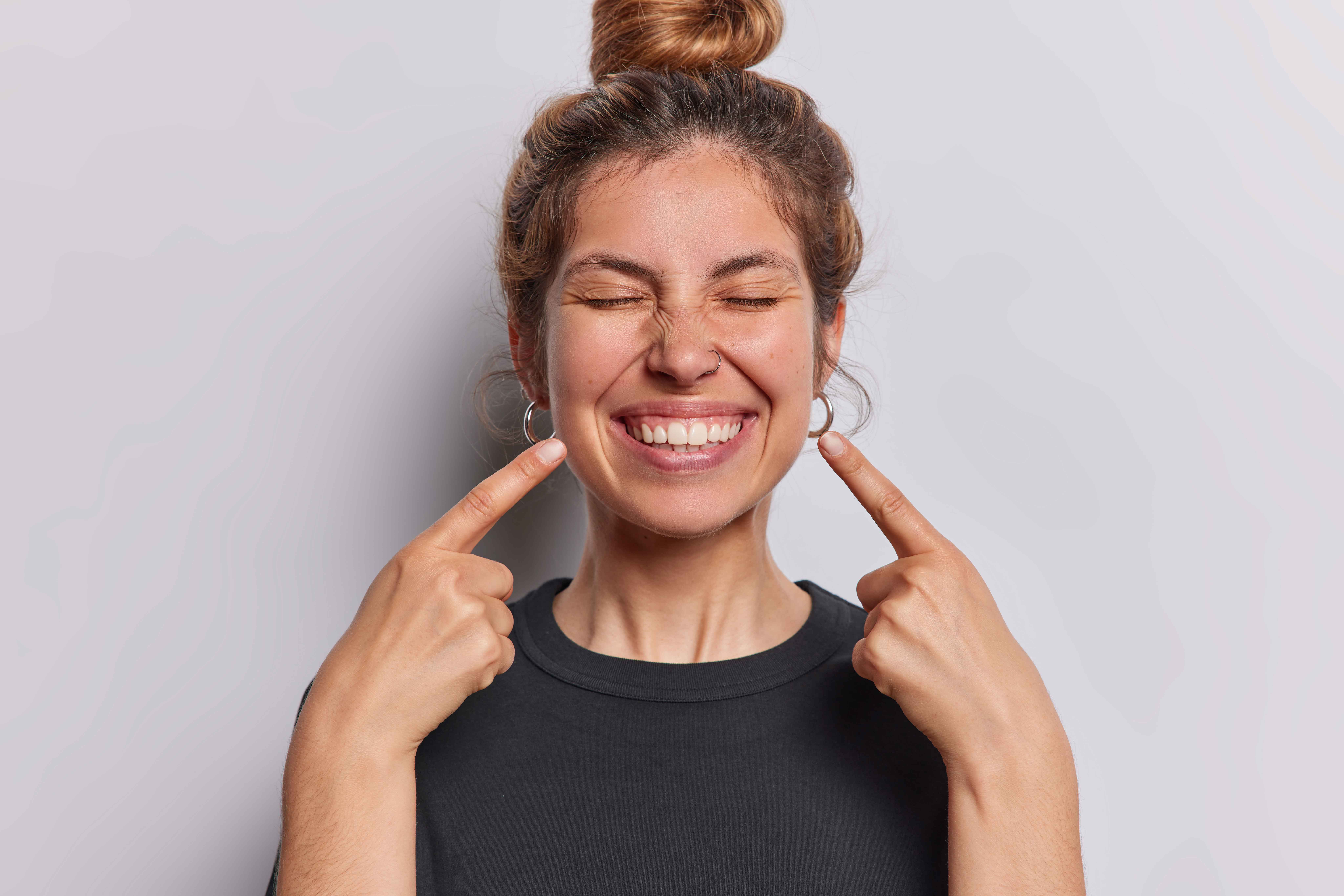 Woman smiling and pointing at her white cavity-free and stain-free teeth