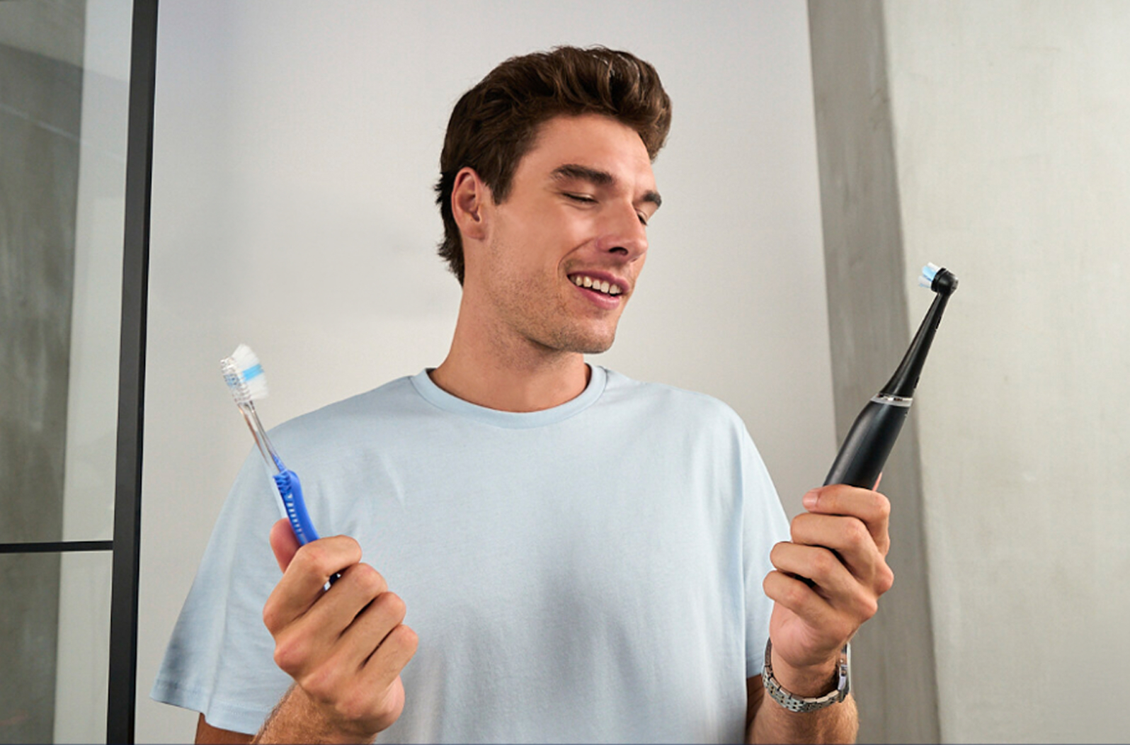 Man holding Oral-B iO electric toothbrush in one hand and a manual toothbrush in one hand.