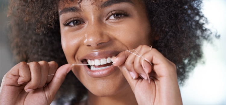 Woman in a bathroom smiling and flossing her white teeth.