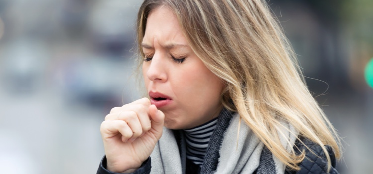 Young woman on the street coughs into her hand.