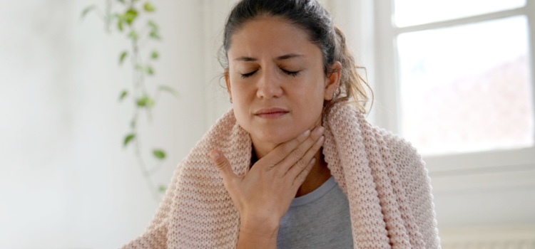 Woman sitting on bed with sore throat