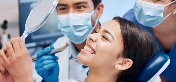 Dentists and female patient smiling into mirror at dental consultation.