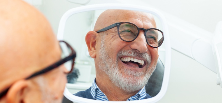 Senior male patient smiling reflection in dental mirror.
