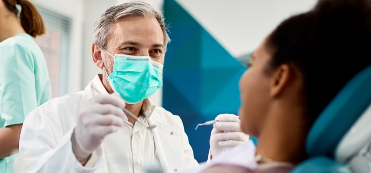 Old male dentist examining young female patient