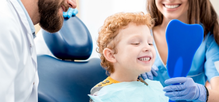 Young boy smiling into mirror at the dentist with his dad and dentist