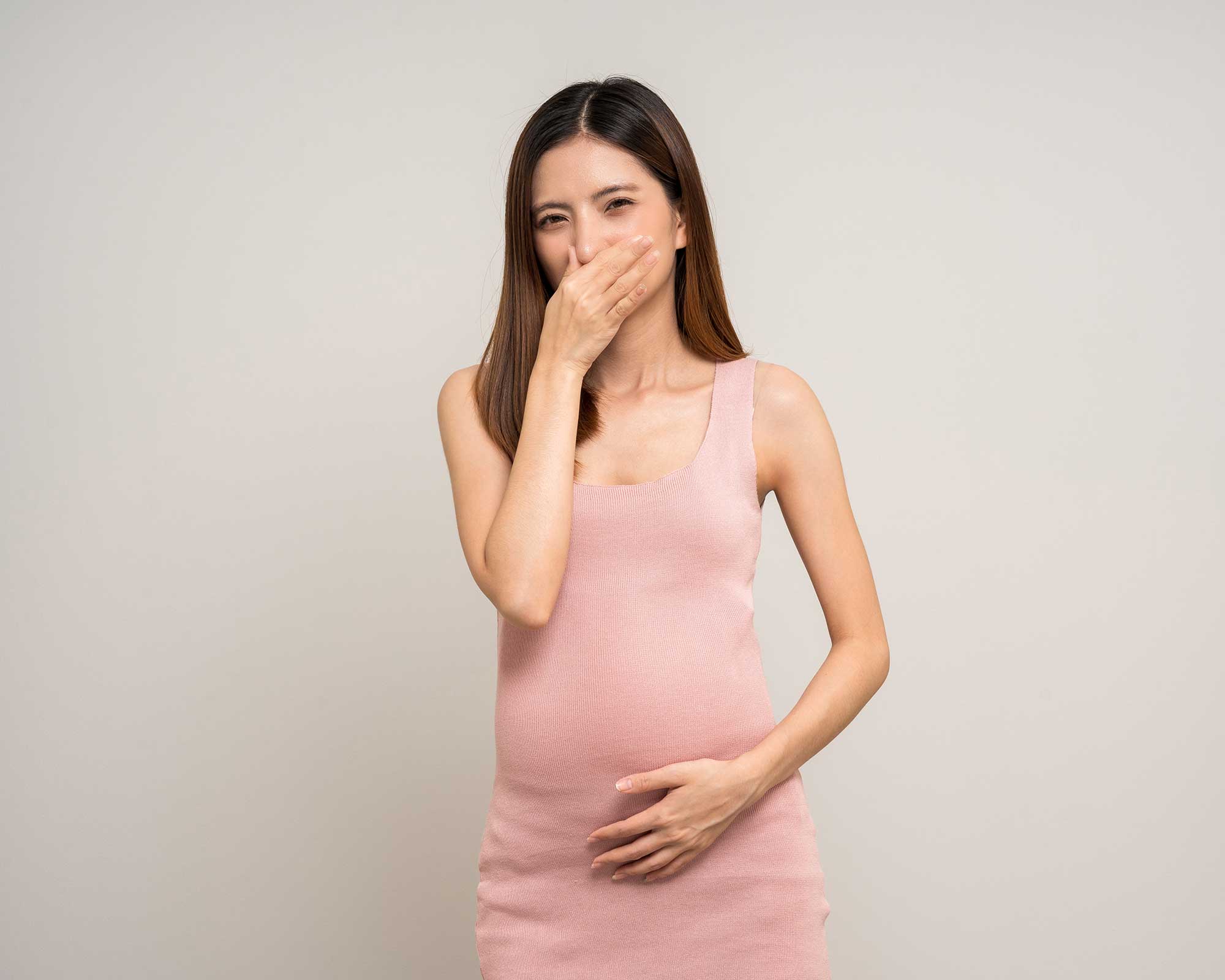 Pregnant woman in pink dress holding her hand against her mouth