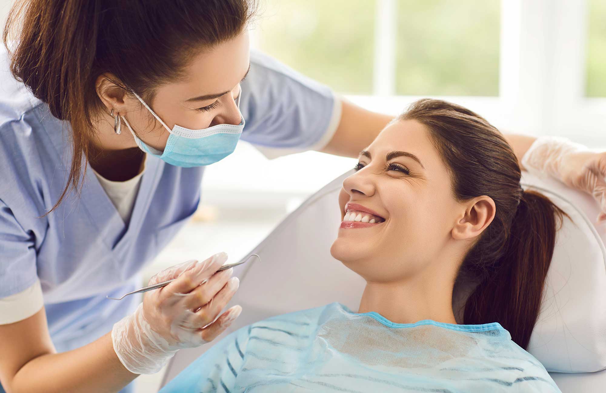 Dental professional holding tool and leaning over a smiling patient