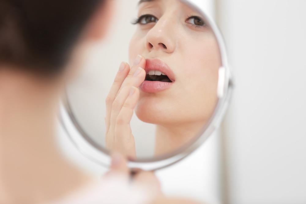 Woman looking in a mirror and touching a cold sore on her lip