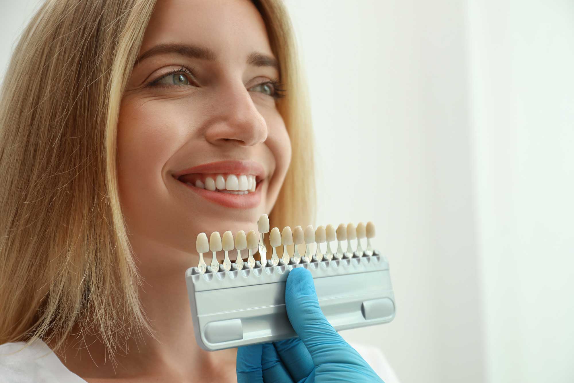 Dental professional holding up a tooth color chart against a patient's teeth