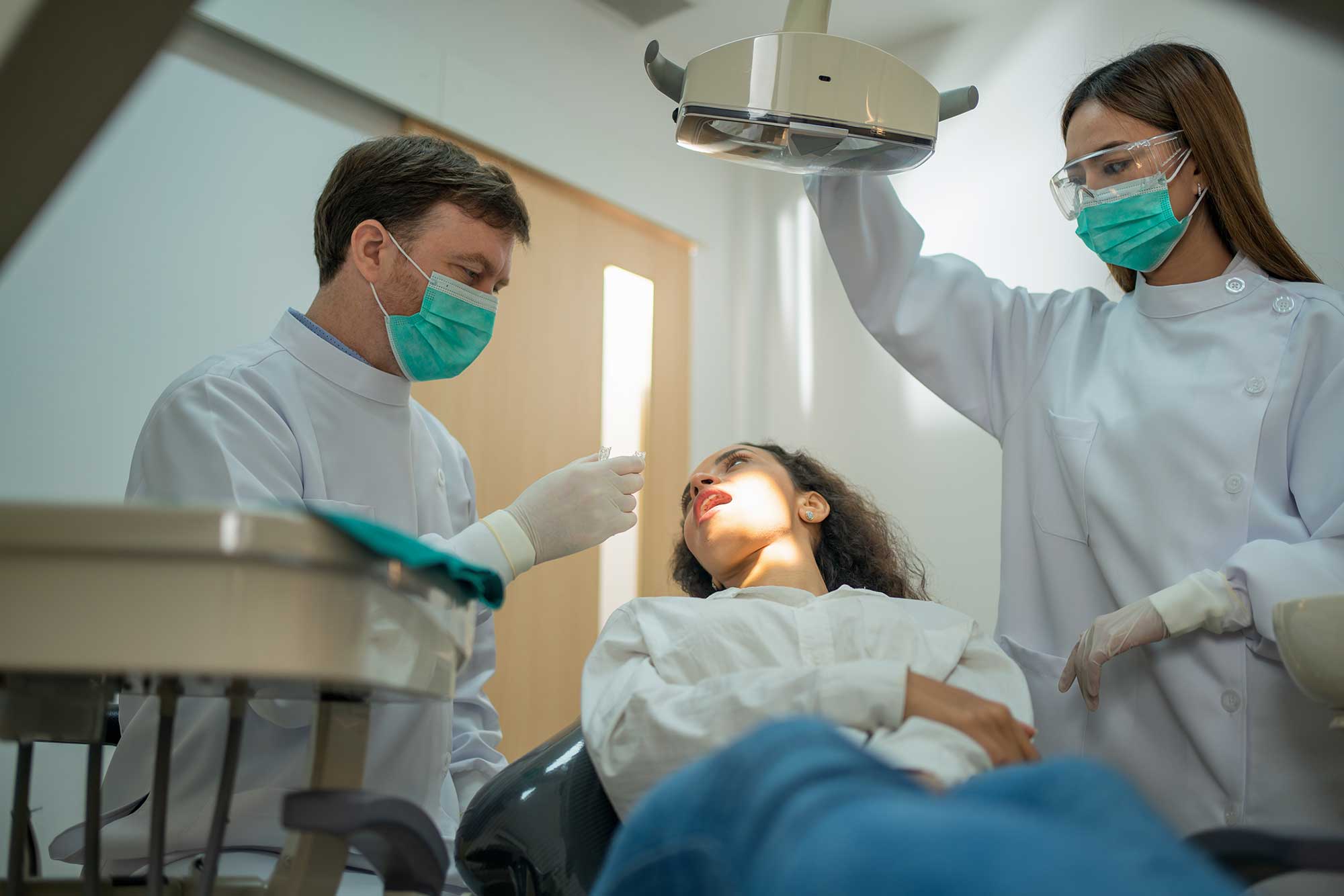 Dentist and assistant examining a patient in a dental clinic, wearing protective masks and gloves