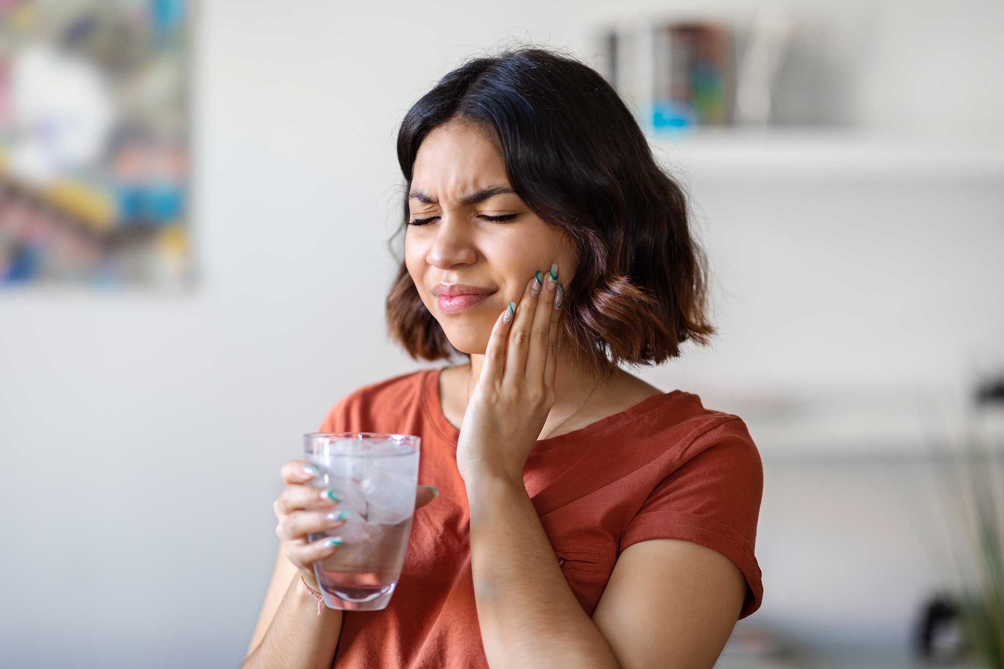 Grimacing woman holding a glass of ice water and holding the side of her face image