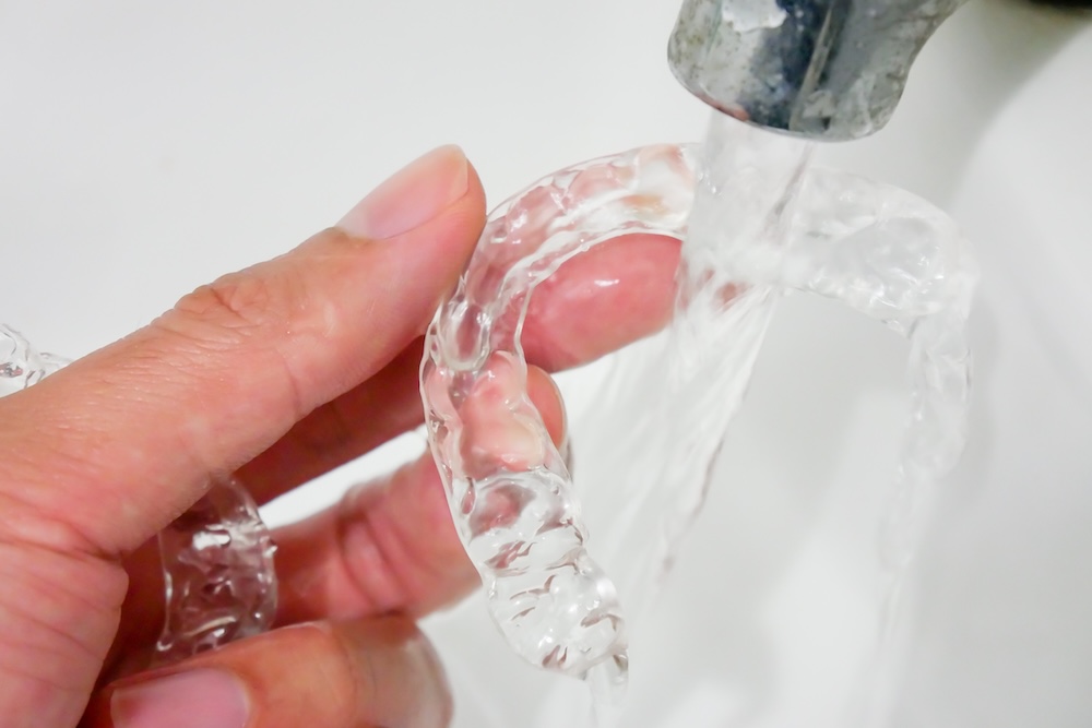Image of clear plastic retainer being rinsed under faucet