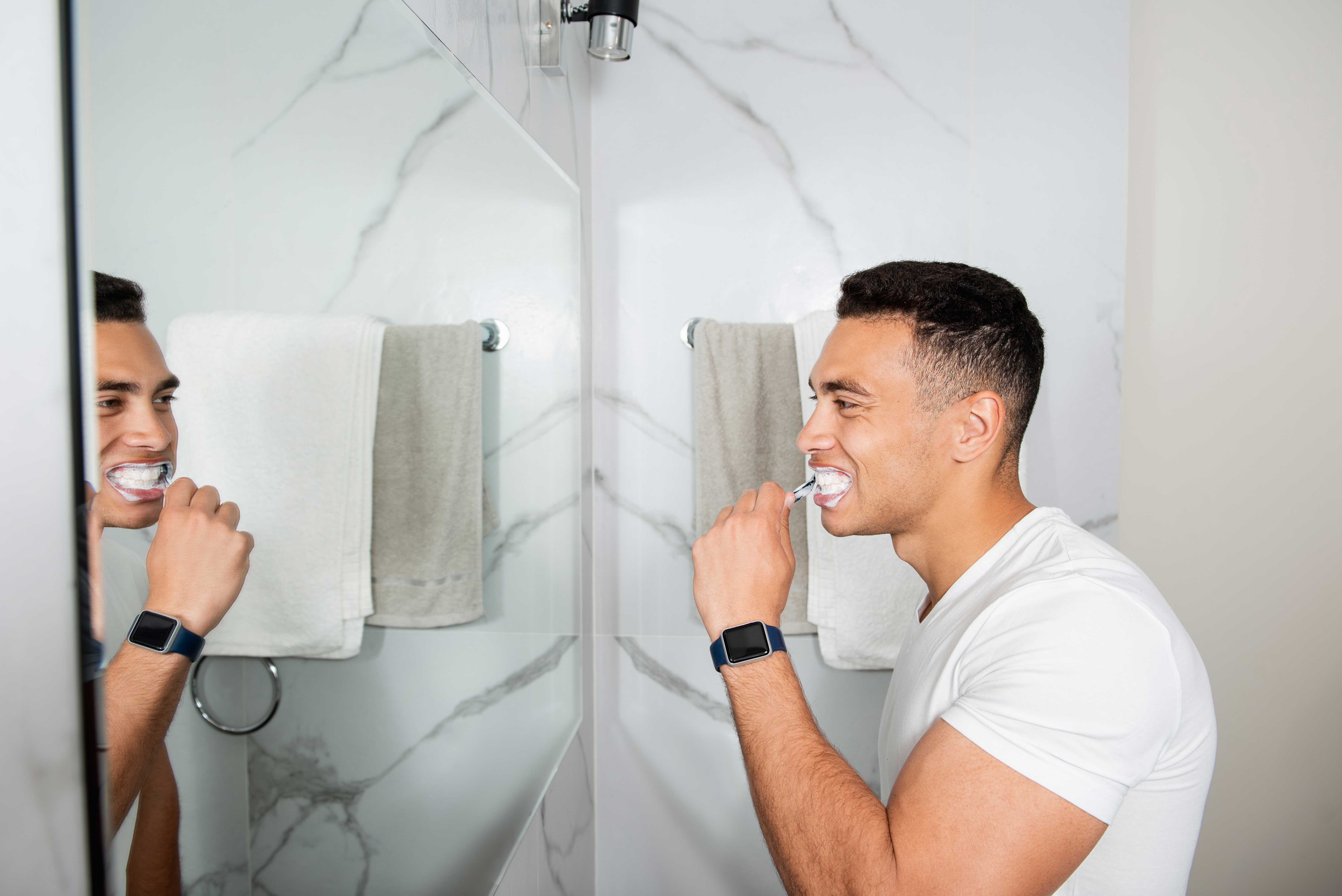 Man brushing his teeth in front of a mirror image