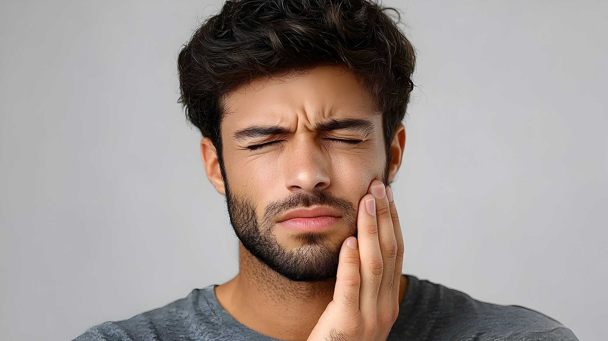 Man experiencing toothache with eyes closed, touching his cheek with his hand, expressing discomfort