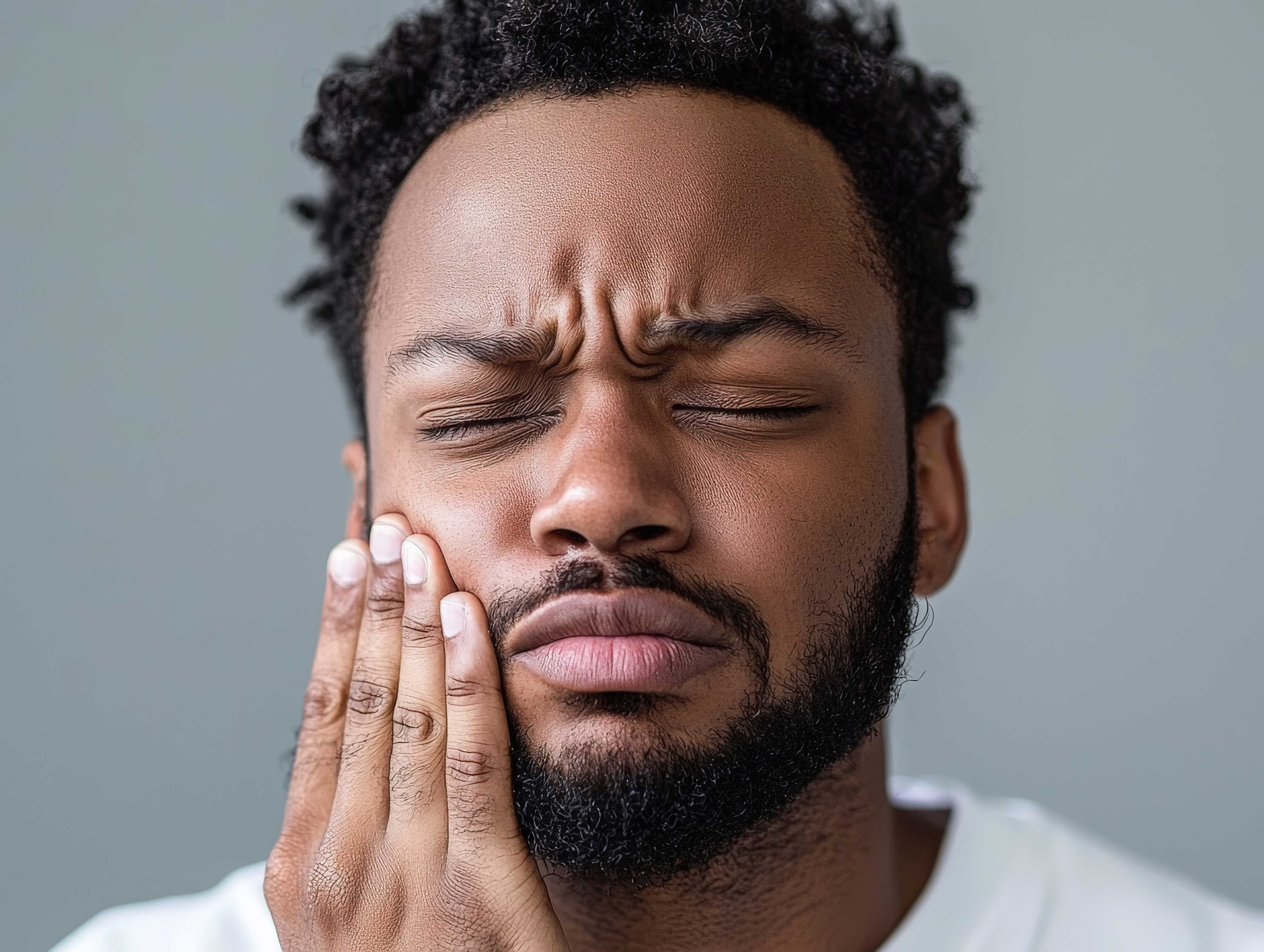 man-holding-his-jaw-and-frowning-like-he-is-in-pain