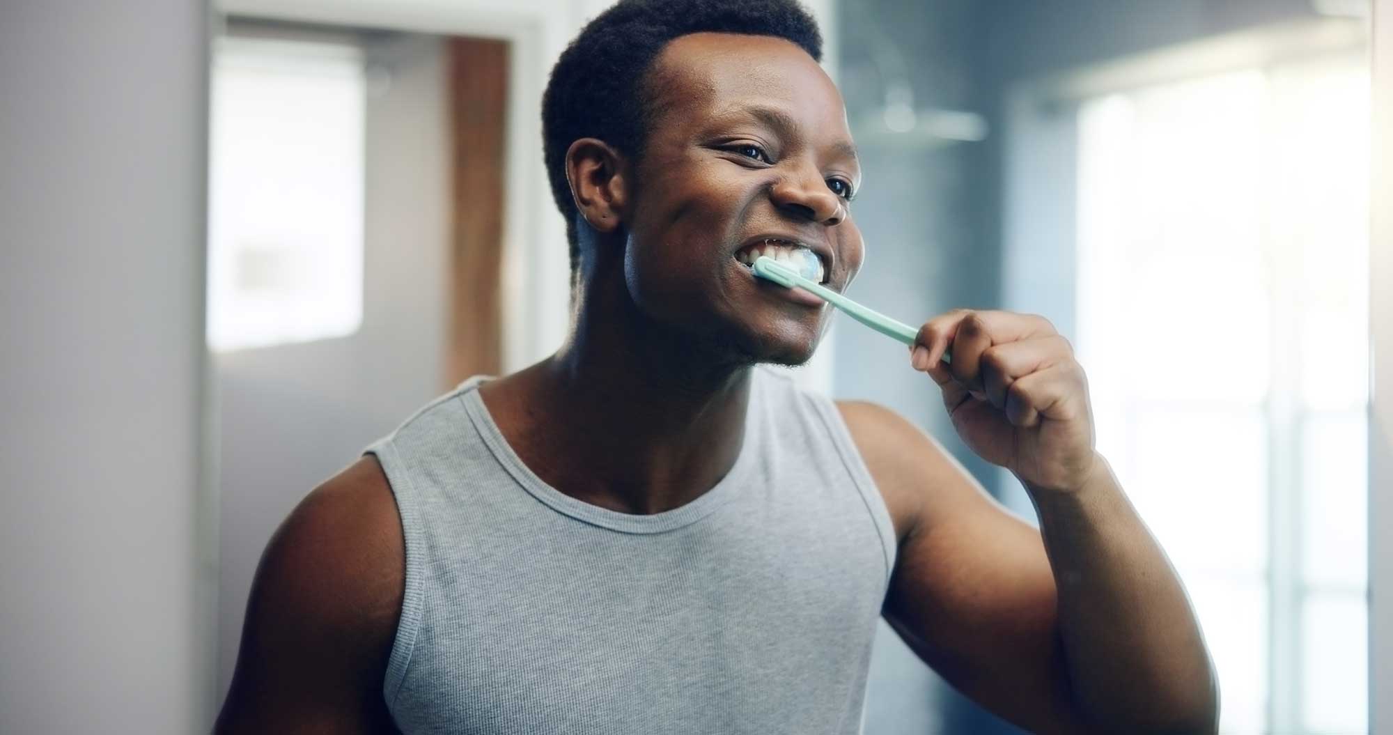 Man smiling and brushing teeth in mirror
