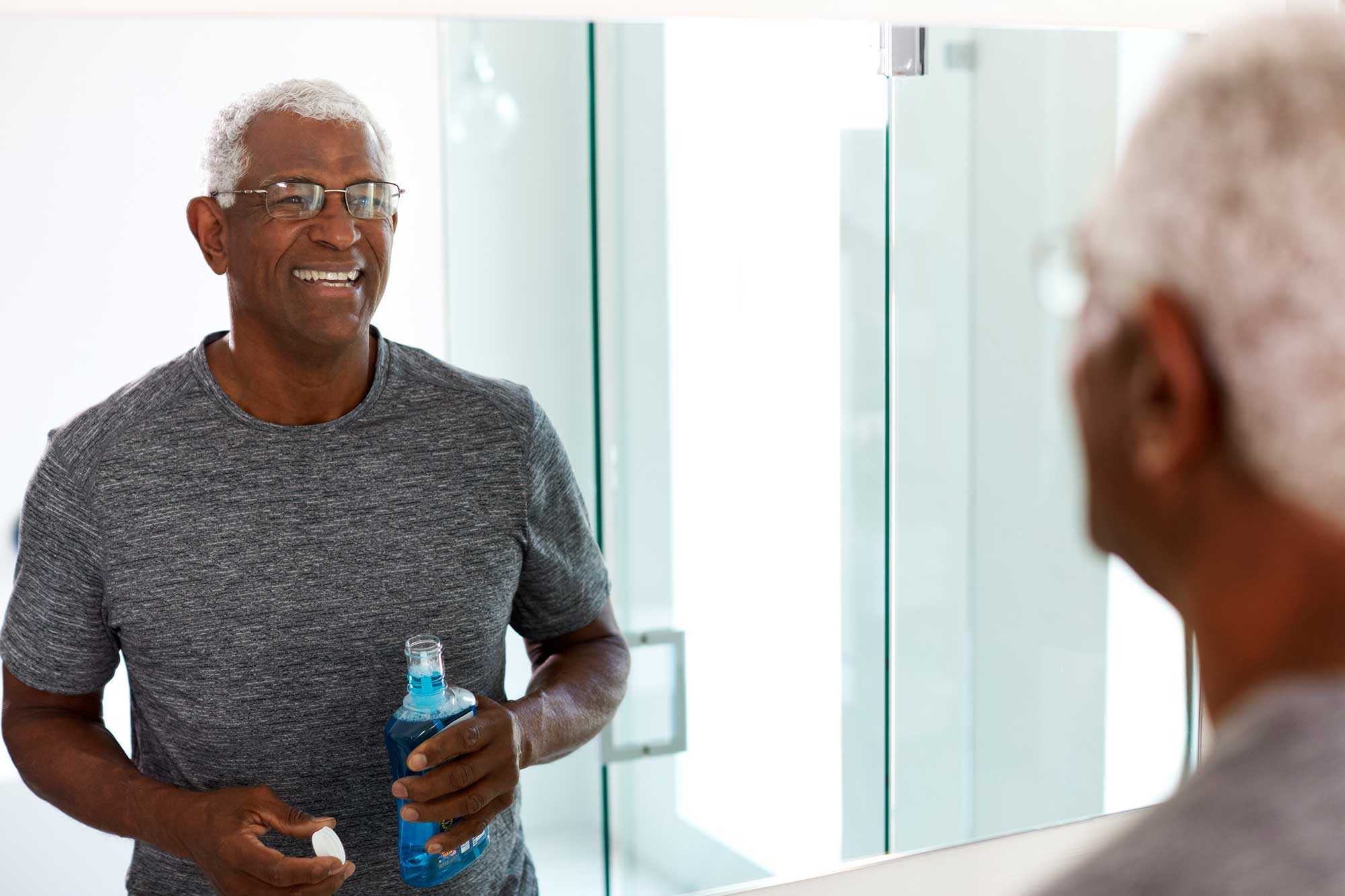 Older man looking in a mirror holding a bottle of mouthwash