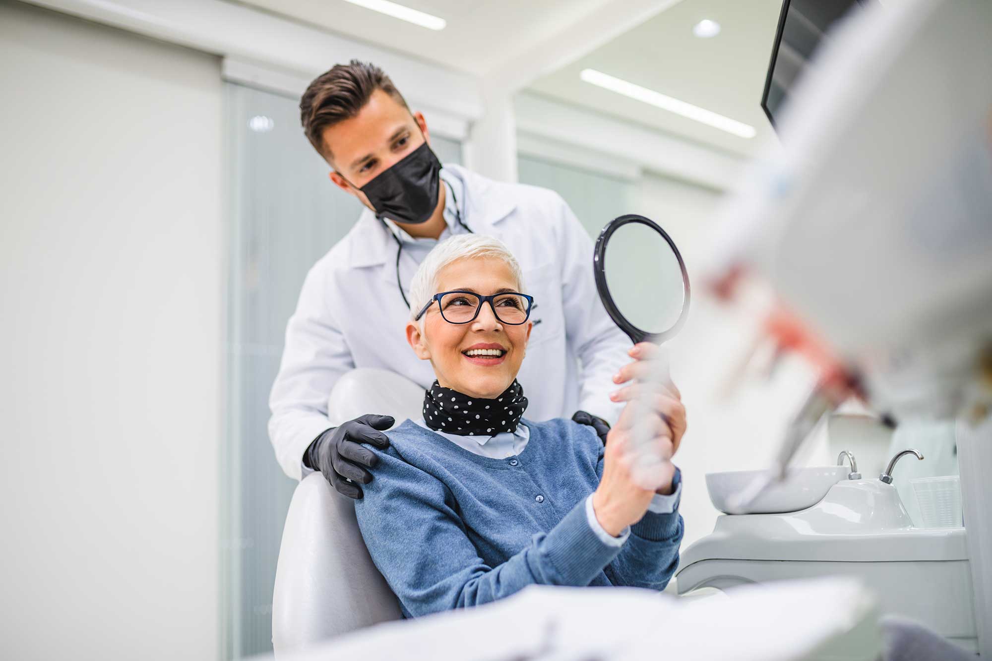 Older woman looking at her smile in a mirror in a dentist’s office image