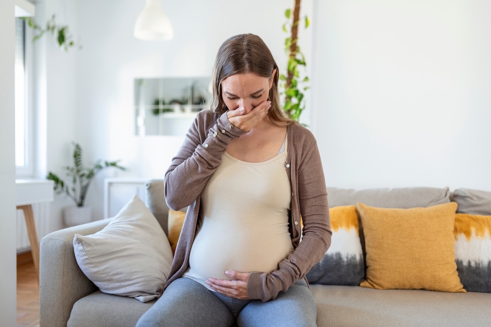 Woman holding her pregnant stomach and experiencing an oral issue Woman holding her pregnant stomach and experiencing an oral issue