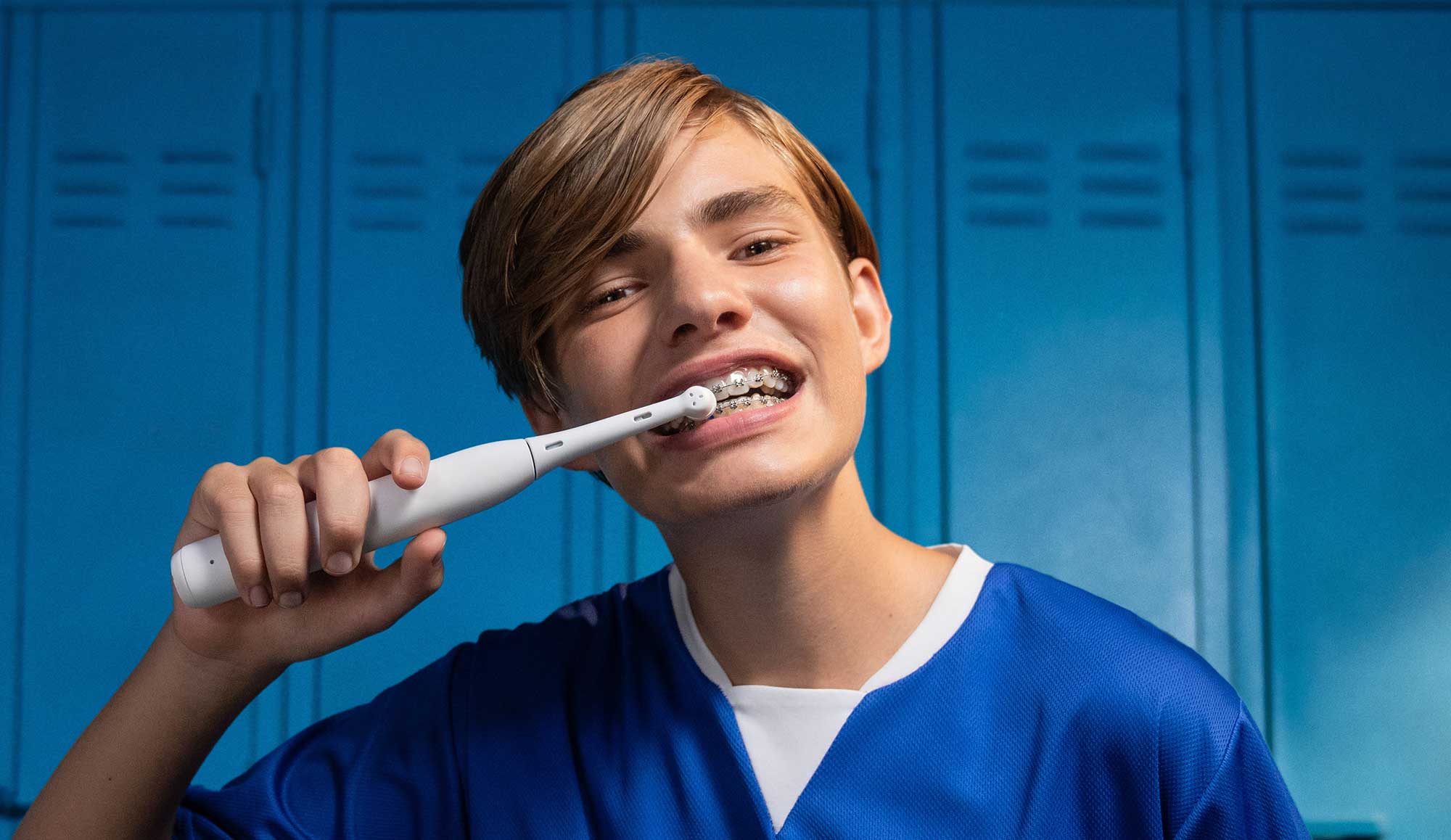 Smiling teen boy with braces brushing his teeth with an electric toothbrush