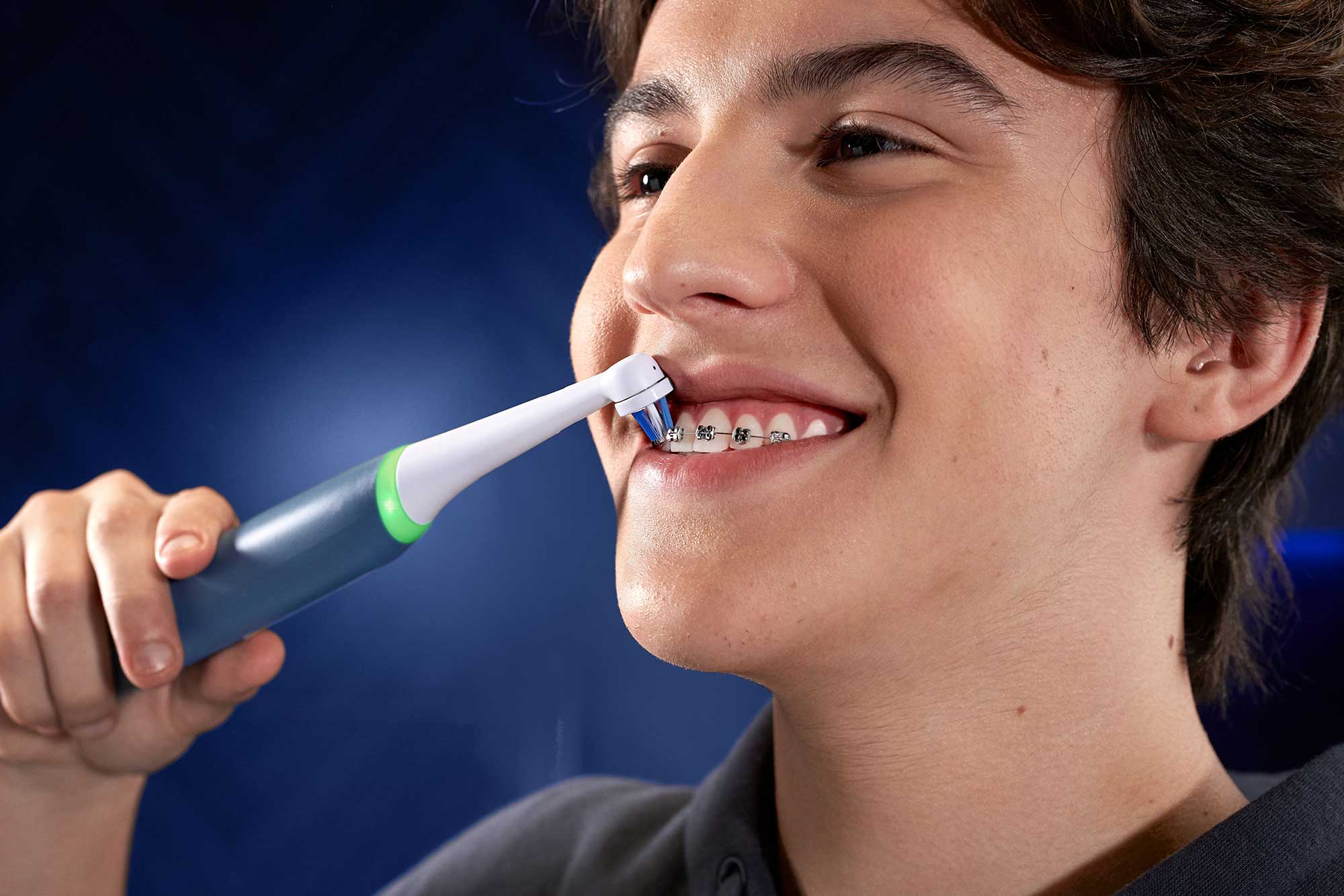 Smiling teen with braces brushing his teeth with an Oral-B electric toothbrush