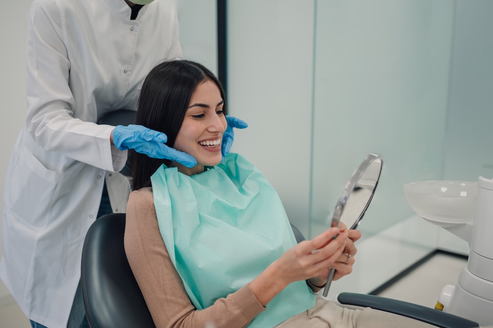 Smiling woman in a dentist office looking at her teeth in a mirror image