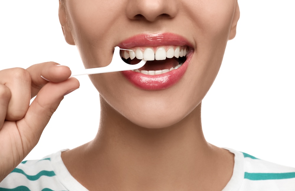 Woman flossing her top teeth with a floss pick