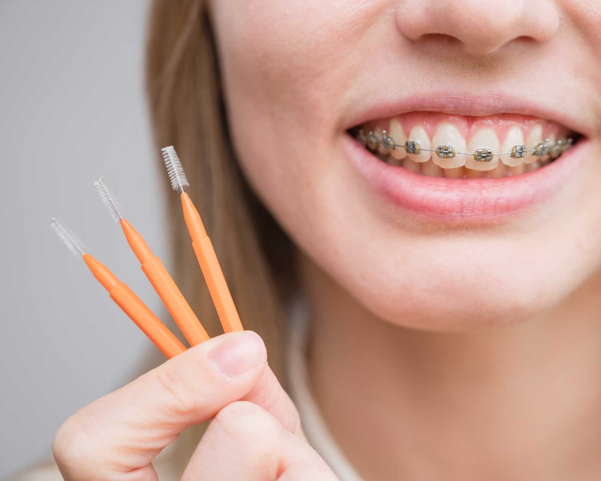 Woman in braces holding up a flossing tool specially designed for braces
