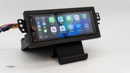 Aftermarket 1.5-DIN touchscreen radio mounted in a custom dash kit for a C5 Corvette, displaying the Apple CarPlay home screen, with wiring harness visible, photographed on a white background.