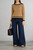 Model wearing tan knit sweater with black trim, styled with wide‑leg dark denim jeans, tan shoes, and a brown leather tote.
