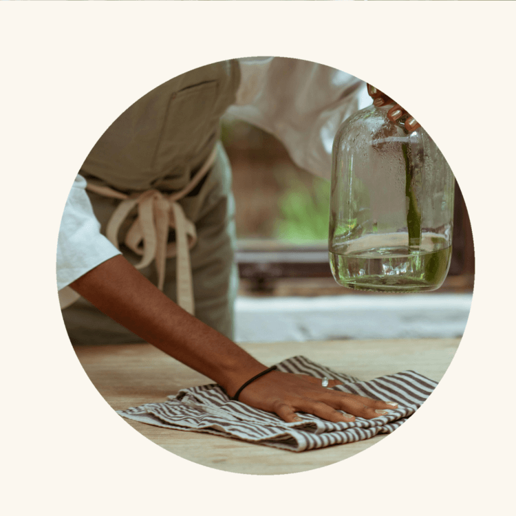 A person in a neutral-toned setting is holding a clear glass bottle with a liquid