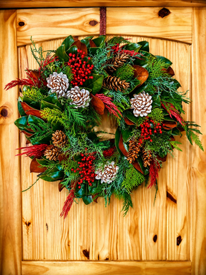 fresh wreath made with cedar boughs and pine cones hanging on a wood door