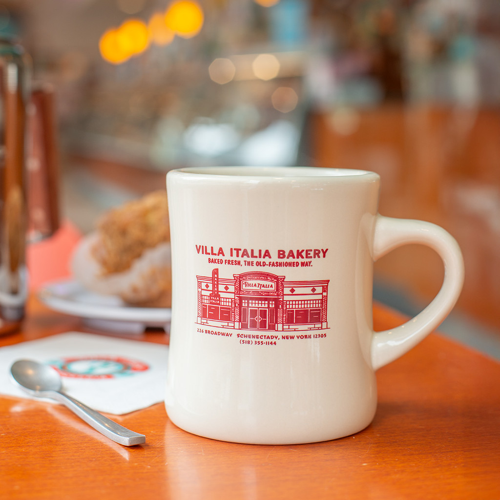 Bring home a piece of Villa Italia Bakery history with our Retro Diner Mug. This heavyweight ivory ceramic coffee mug features a vintage illustration of our iconic Italian bakery in Schenectady, New York — celebrating over 60 years of tradition.

Designed in classic 1950s diner style, this sturdy ceramic mug is perfect for coffee, espresso, cappuccino, or hot chocolate. Whether you’re pairing it with our famous coffee cake or gifting it to a coffee lover, this nostalgic bakery mug adds timeless charm to any kitchen.

• Heavyweight ivory ceramic
• Classic retro diner shape
• Vintage Villa Italia Bakery artwork
• Perfect gift for coffee lovers
• Ships nationwide

Sweet Since ’65.
