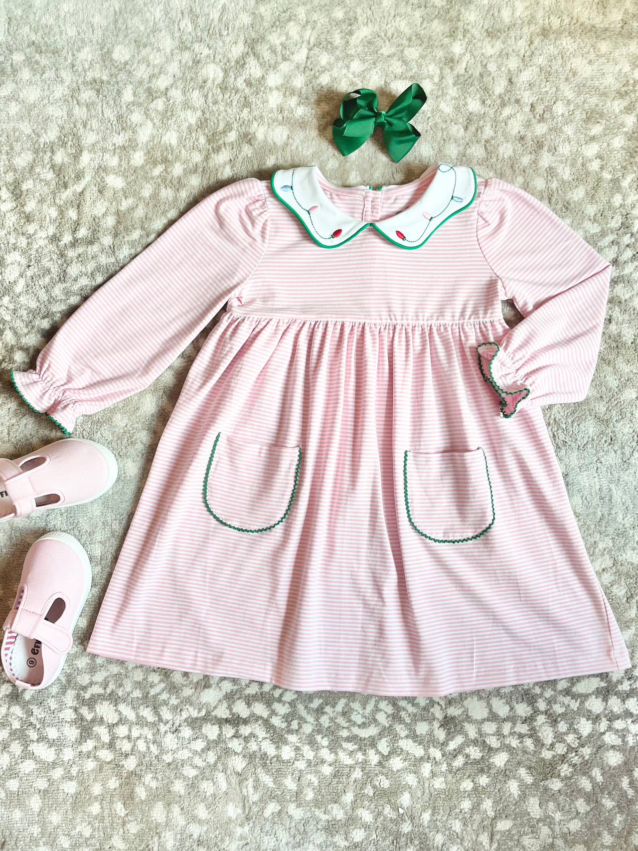 pink and white stripe girls dress with green trim around collar, sleeves and pockets. Collar has embroidered Christmas lights along it's scalloped edge.