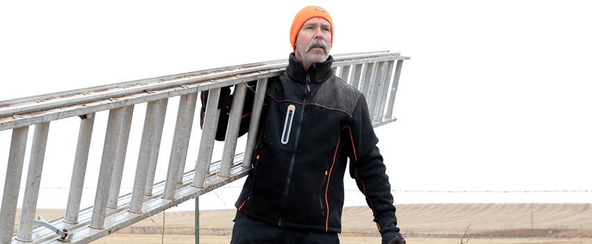 Man carries ladder over his shoulder while wearing an abrasion-resistant winter work coat.