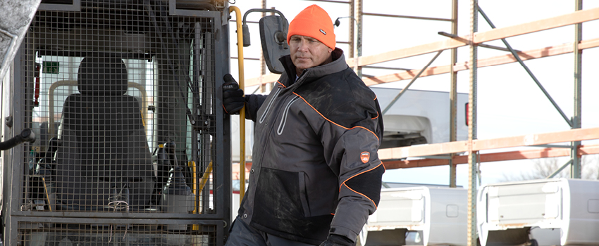 Man wearing insulated work coat operated heavy equipment.