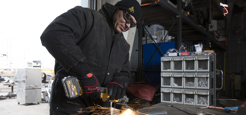 Man wearing insulated coveralls uses a grinder hand tool in extreme cold weather.