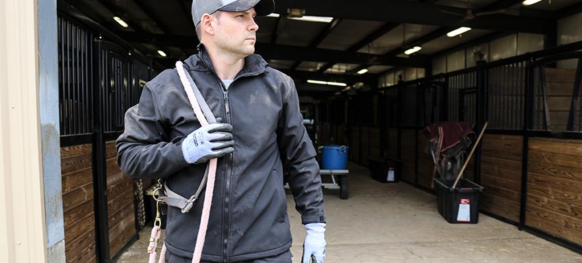 Man wearing all weather jacket works in horse barn.