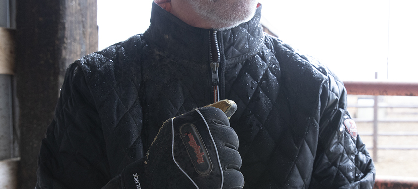 Man wearing all weather jacket works in horse barn.